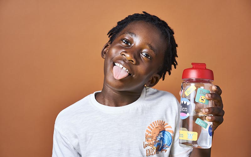 Boy holding a water bottle with waterproof name stickers from My Nametags, on a brown background