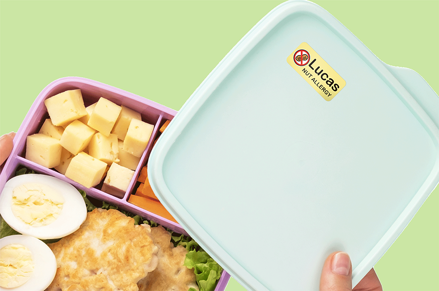 A blue lunchbox with a "Nut Allergy" name label slightly open to reveal healthy foods.