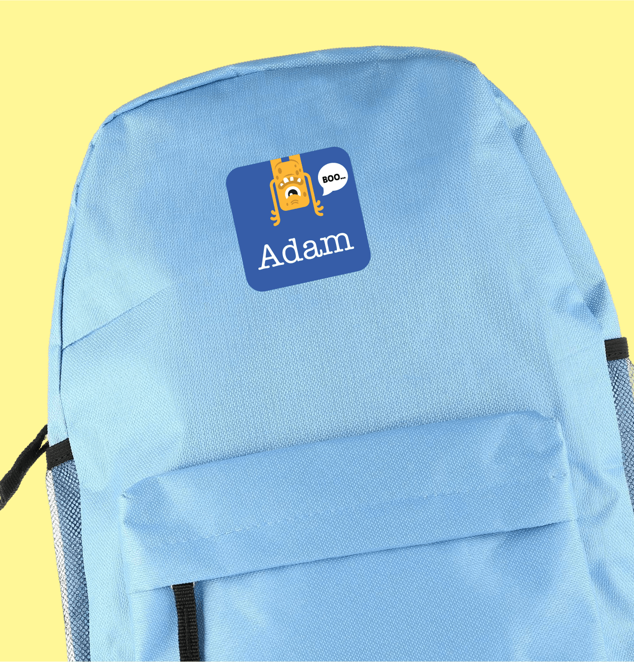 Light blue backpack featuring a playful sticker with an orange cartoon monster saying "Boo" and the name "Adam Smith" underneath, creating a whimsical tone.