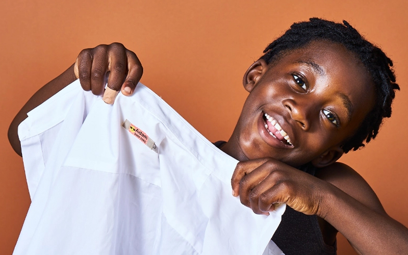 Young boy holding a shirt with My Nmatags iron on label attached, on an orange background