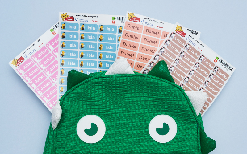 Sheets of My Nametags sticker labels and a green backpack on a grey background