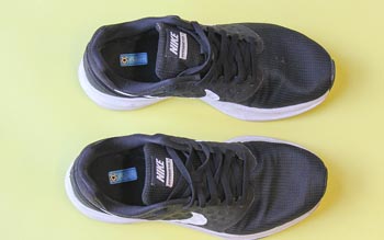 Black kids' trainers with name labels on a yellow backround