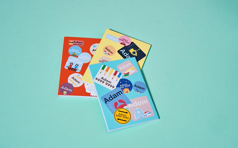 Books with a variety of My Nametags name stickers stuck on, on a blue background