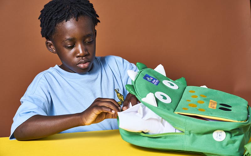 Boy with a green backpack with My Nametags name stickers for school, on a brown background