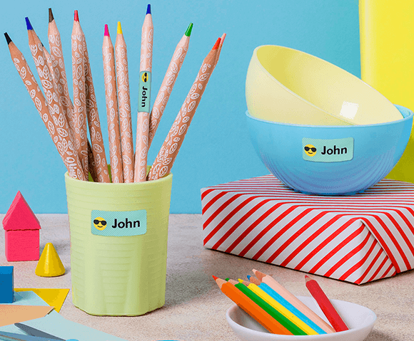 My Nametags colour sticker name labels on a bowl and pencils in a cup, on a blue and yellow background